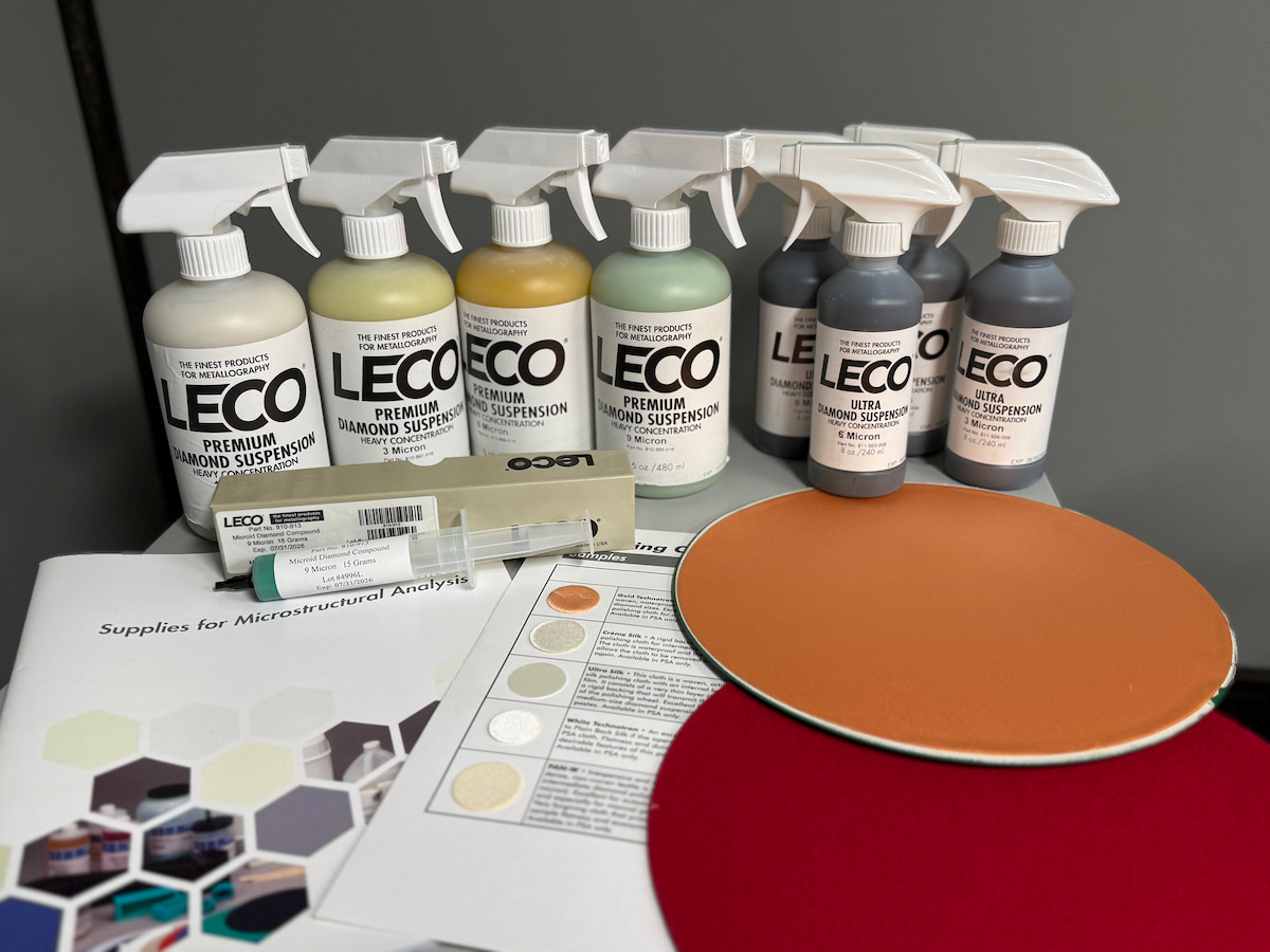 Several bottles of LECO's Diamond Suspensions lined up behind a few polishing cloths and a catalog for microstructural analysis supplies. All supplies used for aluminum analysis.