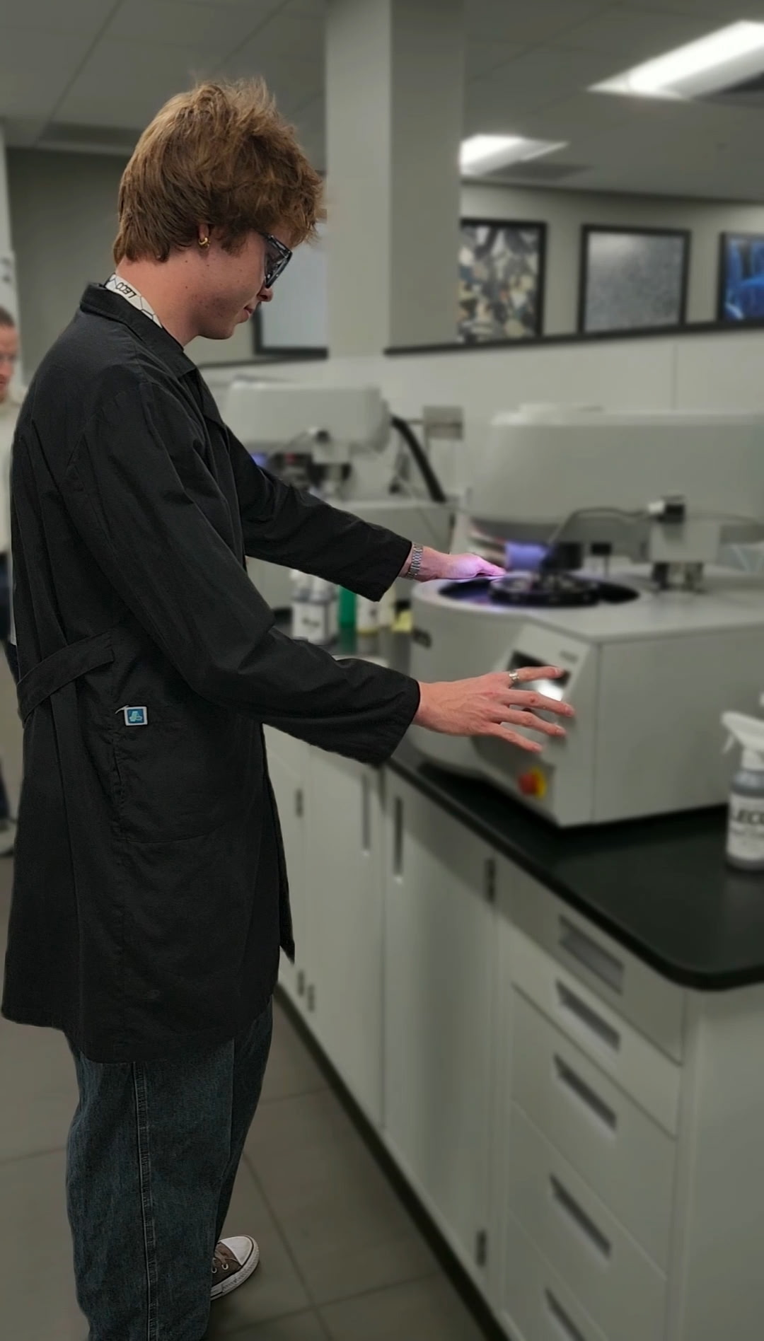A young man with his hands on a LECO polisher/grinder, focused on his work